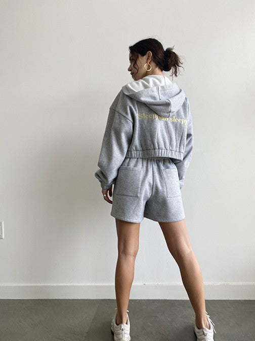 Tell it how it is with our Sleepy and Sleepy Embroidered Zip Up Hoodie! This relaxed fit, cropped hoodie is just made for lounging in, yet perfect for throwing on when you're running out the door. Made with the softest fleece fabric and complete with the sweetest yellow embroidery, this set is guaranteed to be a favorite all year long. Our Sleepy + Sleepy Embroidered Zip Up Hoodie is shown here with our Sleepy + Sleepy Embroidered Sweat Shorts.